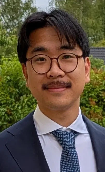 Mörkhårig man med glasögon och mustasch iklädd blå kavaj, vit skjorta och blårutig slips.