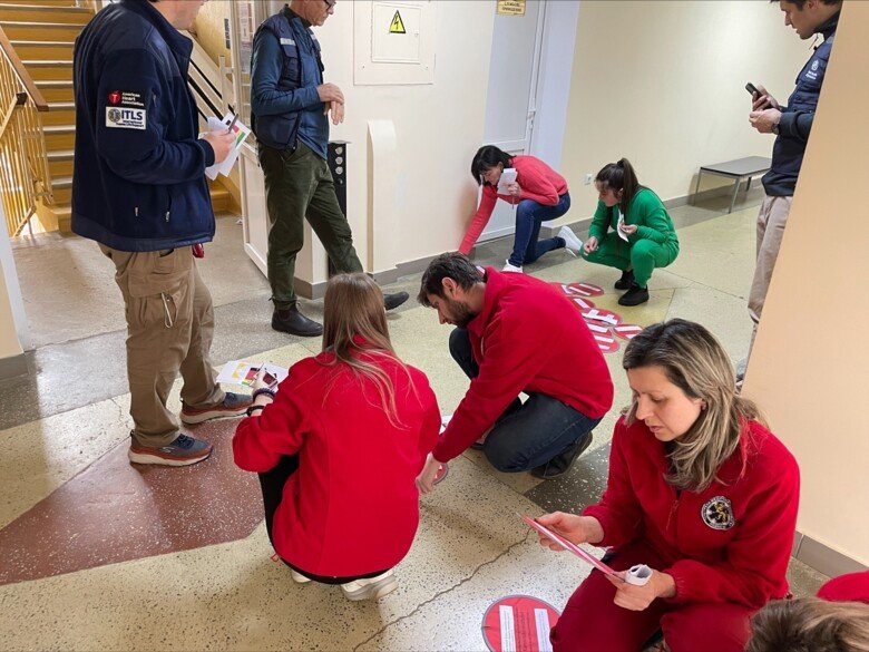 En grupp personer står och sitter på golvet och studerar röda runda plattor