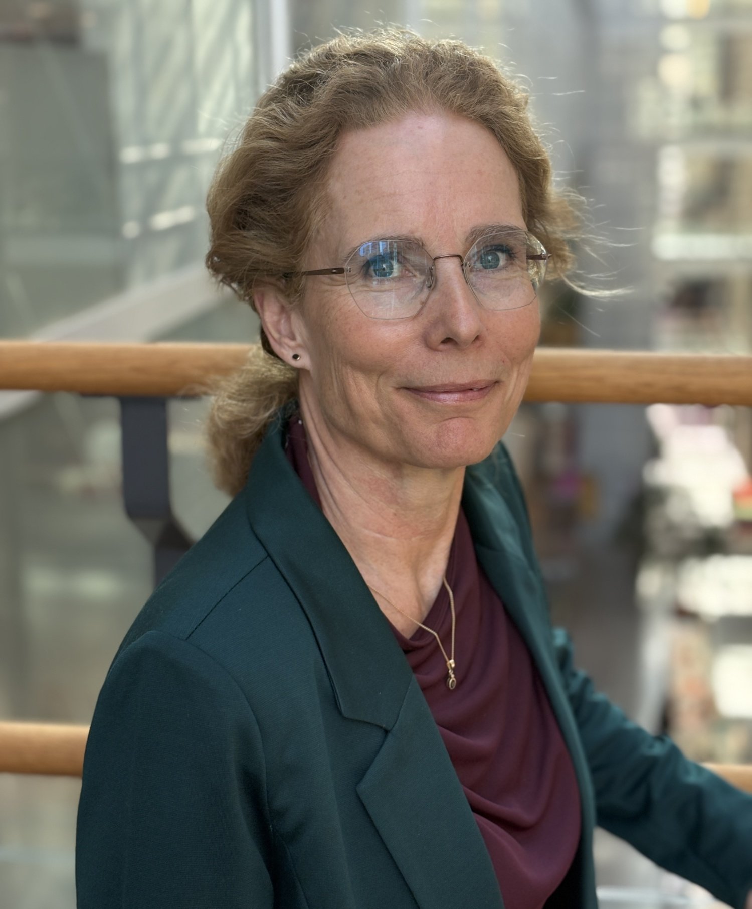 Porträtt på kvinna i grön kavaj och glasögon.