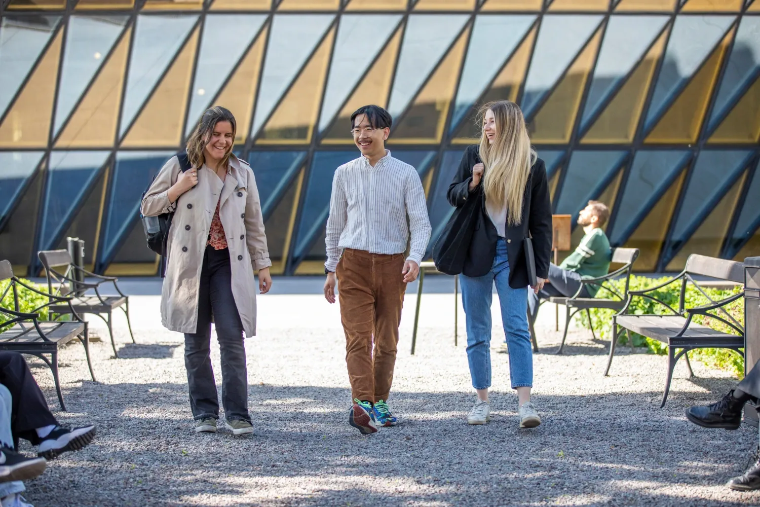 Studenter utomhus på campus Solna en solig vårdag 2022. || Studenter utanför Aula medica || Tre studenter går från campus. Aula medica syns i bakgrunden.