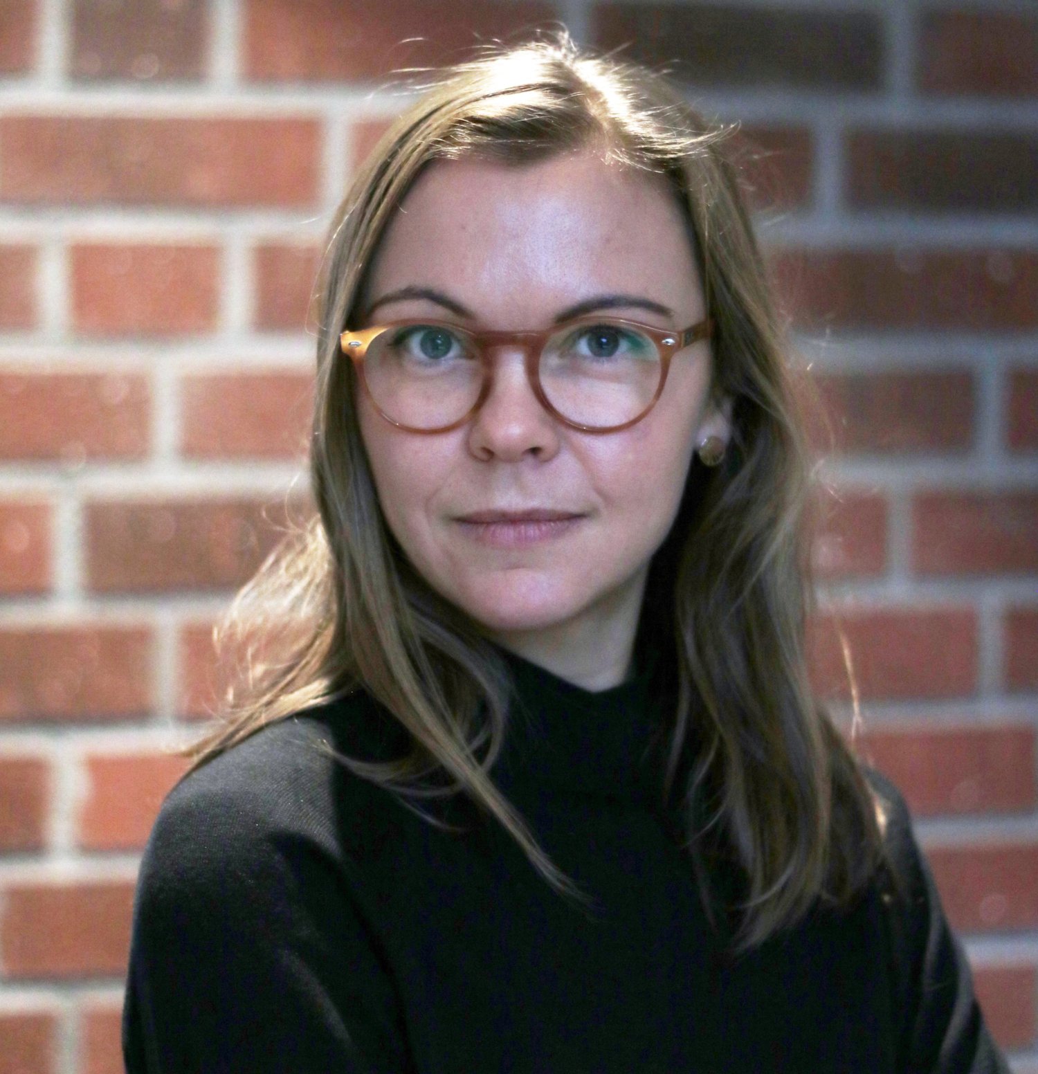 porträtt av kvinna framför tegelvägg.