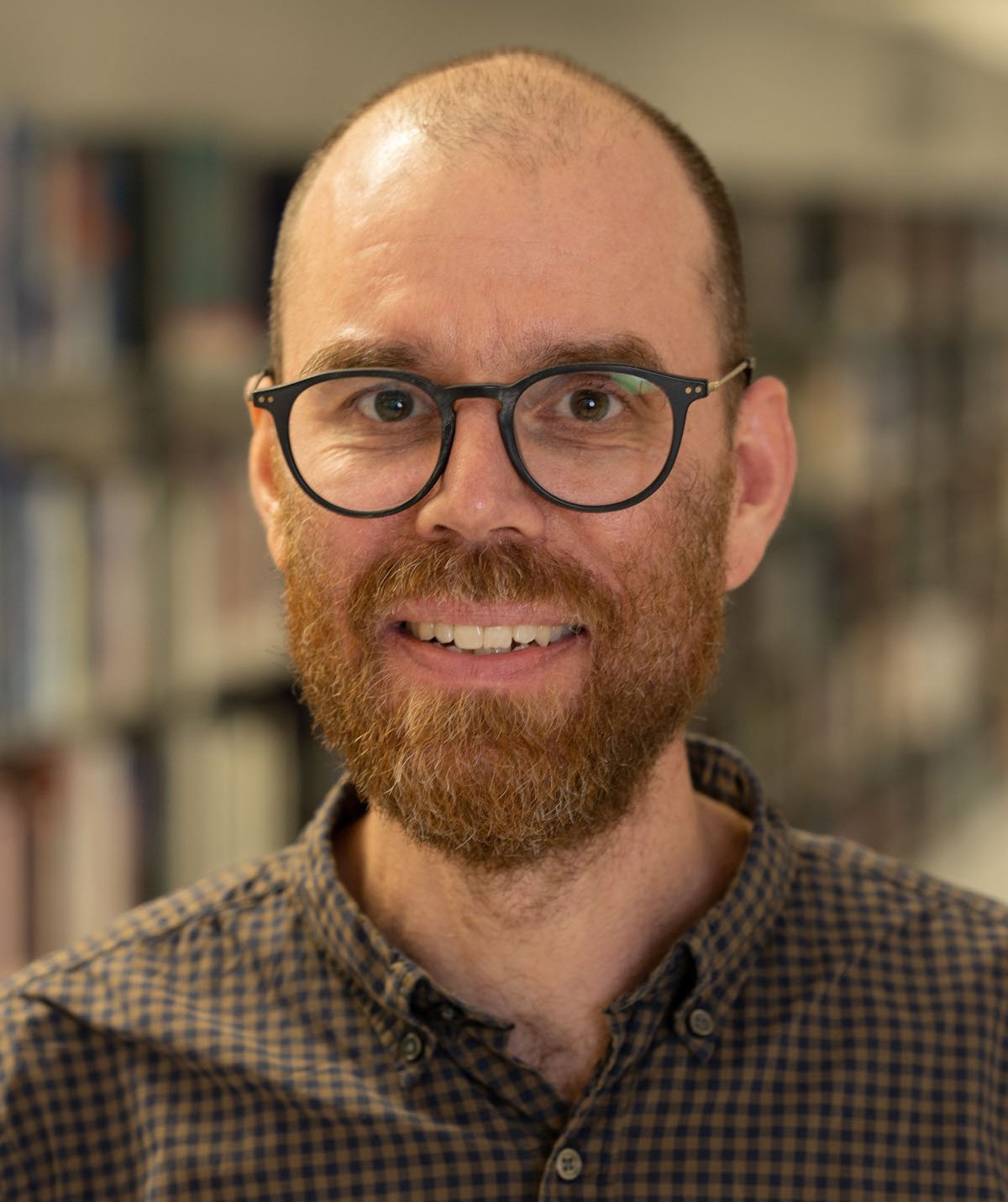 Porträtt av Erik stående framför bokhyllor i ett bibliotek.