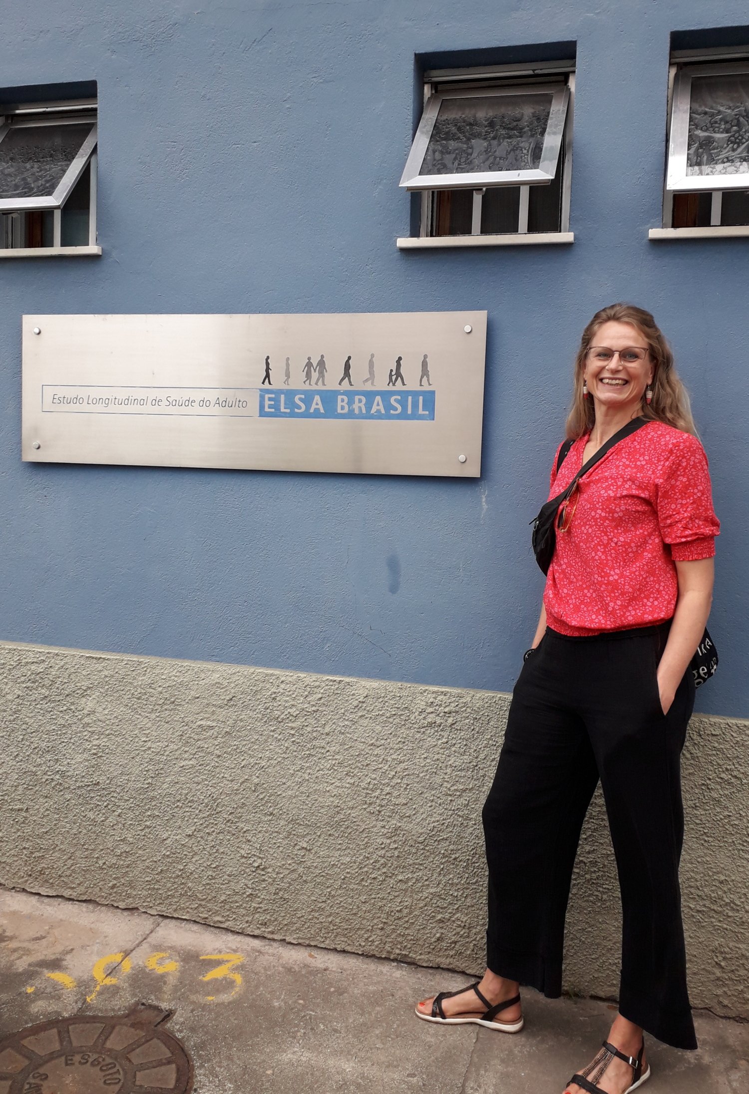 Pernilla står lutat mot byggnaden s blåa vägg och intill en skylt.