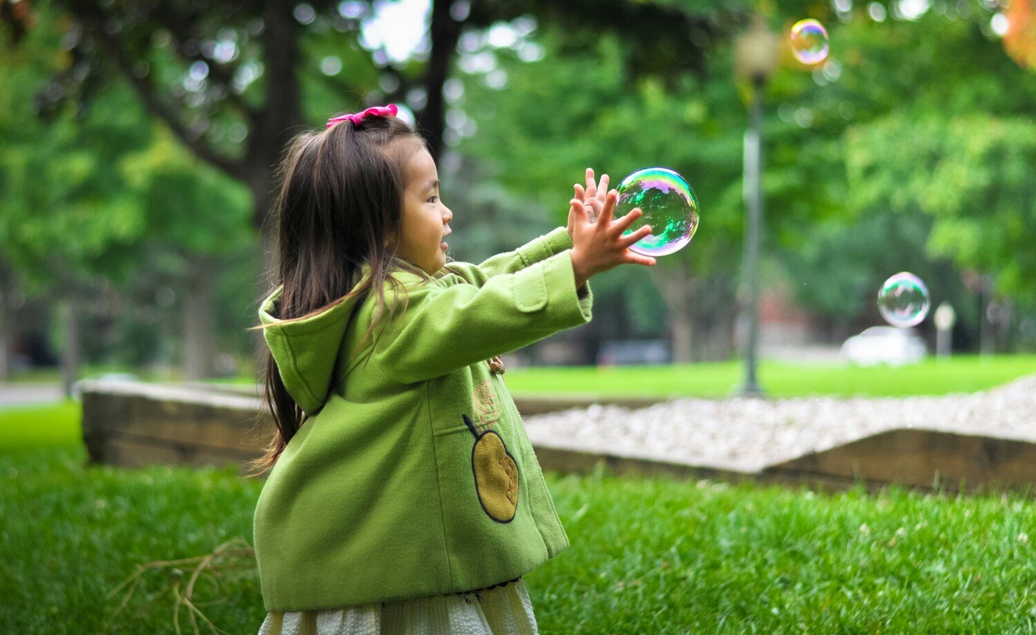 Flicka i grön kappa leker med såpbubblor