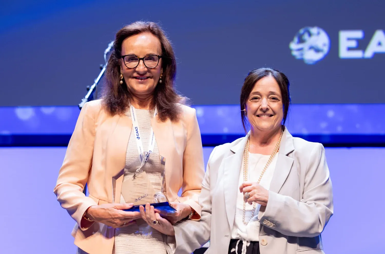 Marianne van Hage tar emot EAACI 2025 award på en scen utav Maria Torres.