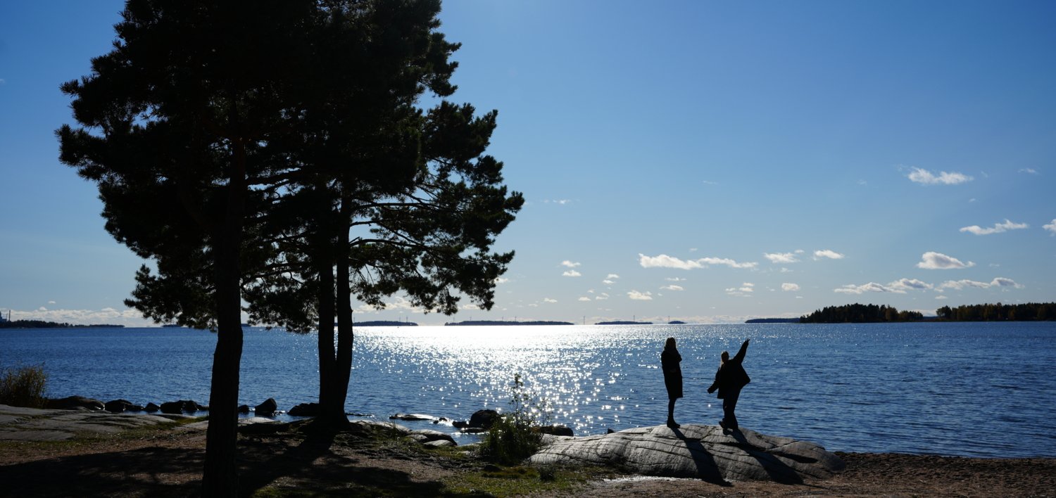 En naturbild vid Värnen en solig dag och två personer som håller handen och hoppa upp i luften.