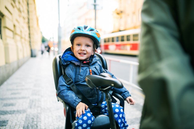 Liten pojke med cykelhjälm ler i sin barnstol.