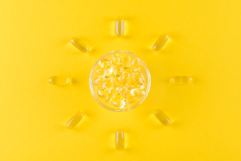Symbolbild för D-vitamin med vitaminkapslar utlagda som solens strålar mot gul bakgrund.