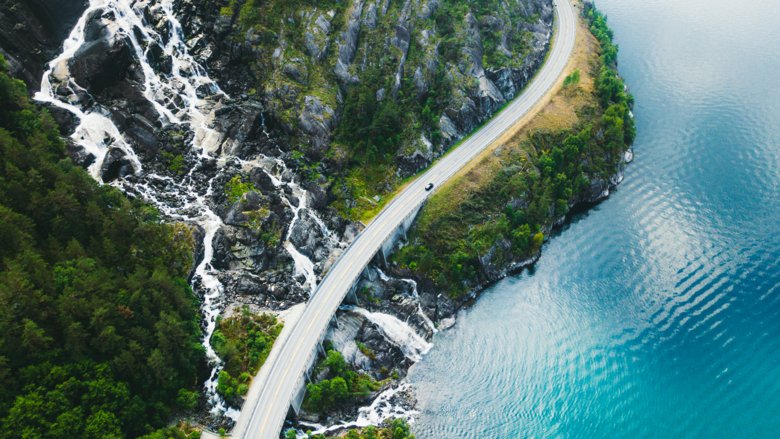 Panoramabild av bil som kör genom pittoresk väg ovanför det enorma vattenfallet nära fjord i södra Norge.