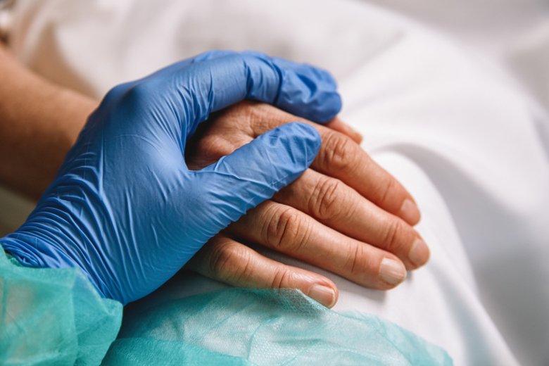 Sjukvårdspersonal med skyddshandske håller sin hand över en patients hand.