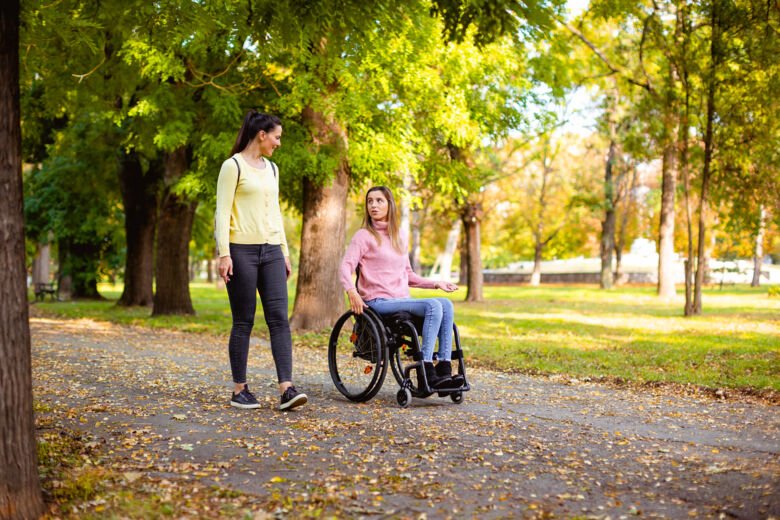Två kvinnor går i en park. Den ena sitter i rullstol.
