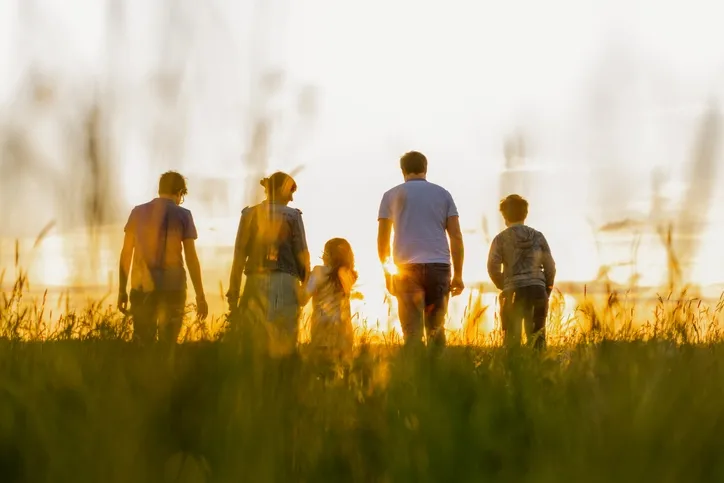 En familj som håller varandra i handen medan de går längs en strand mot vattnet, sett bakifrån.