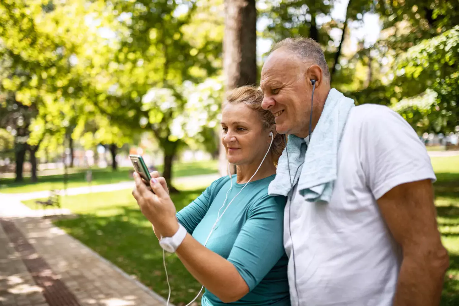 Ett par i övre medelåldern som tittar på en mobil med hörsnäckor i öronen. De står i en park.
