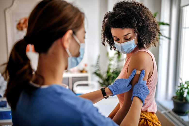Kvinna med munskydd får ett plåster på armen av en sjuksköterska.