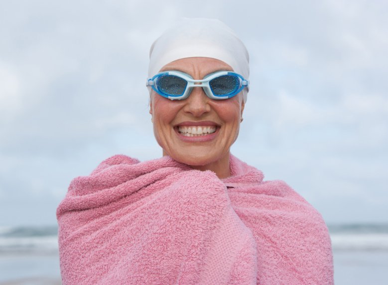 Glad kvinna med simglasögon och badlakan över axlarna har just kommit upp ur havet.