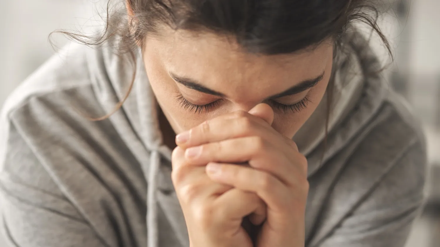 Person med händerna knäppta framför ansiktet, huvudet böjt.