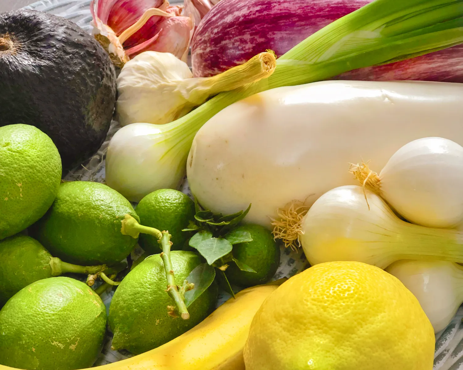 Dekorativ bild av Närbild på färgglada frukter och grönsaker, inklusive limefrukter, citroner, auberginer, avokado, bananer, vitlök och salladslök.