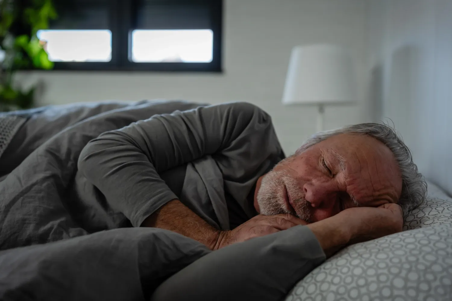 Äldre man som sover i en säng, på sidan.