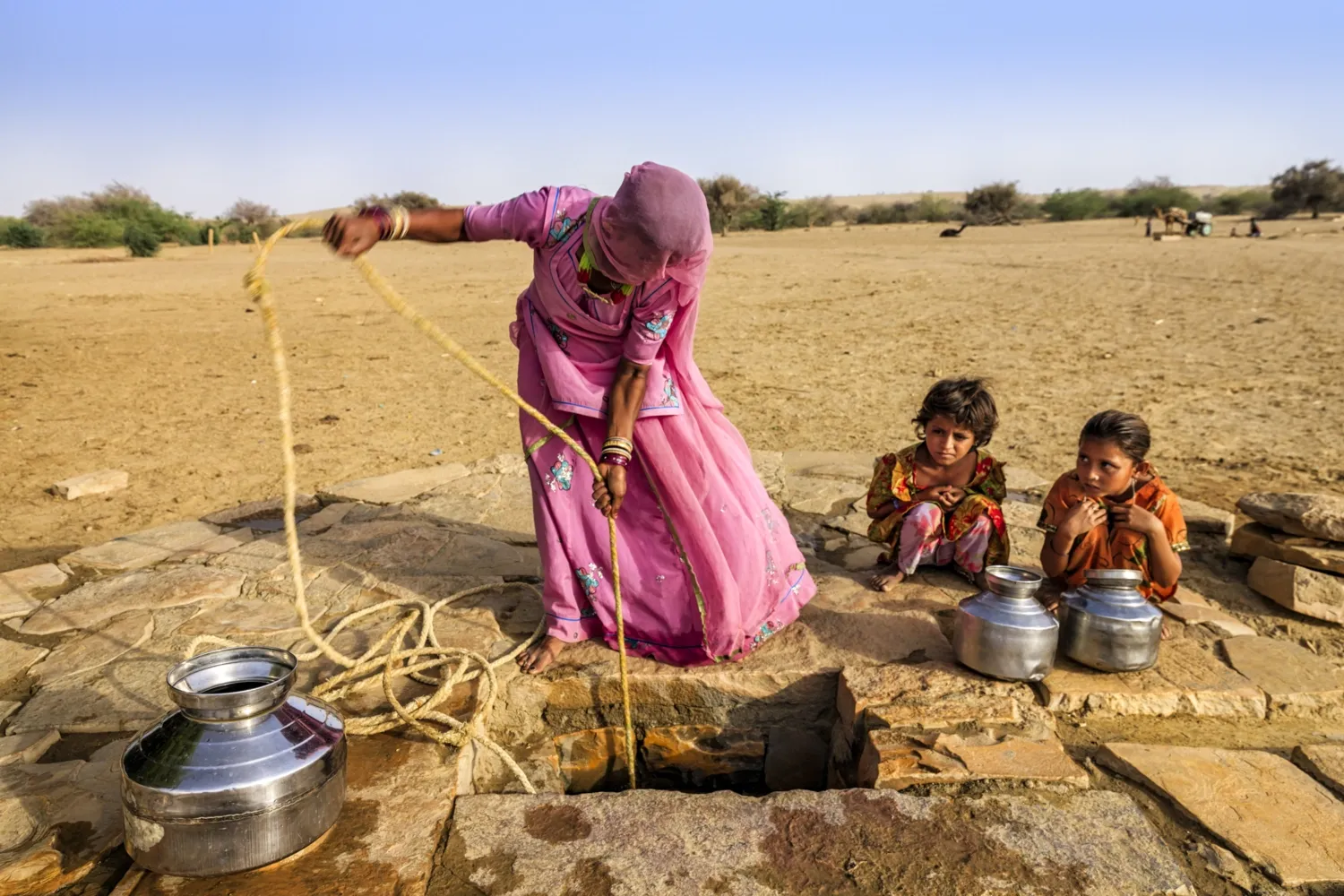 Kvinna hämtar vatten hinke genom en brunn.