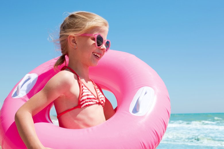 Glad flicka på stranden med rosa simring.