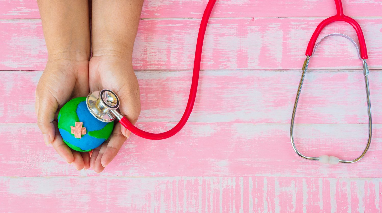 Symbolisk illustration: händer som håller i ett jordklot, som undersöks med stetoskop.