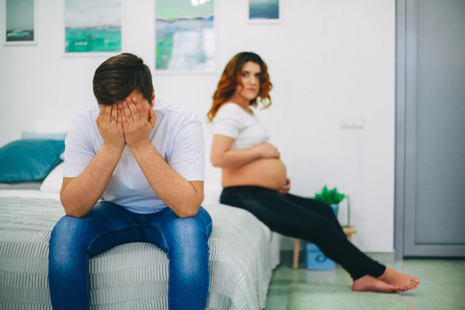 En gravid kvinna i bakgrunden med ångestfylld man i förgrunden