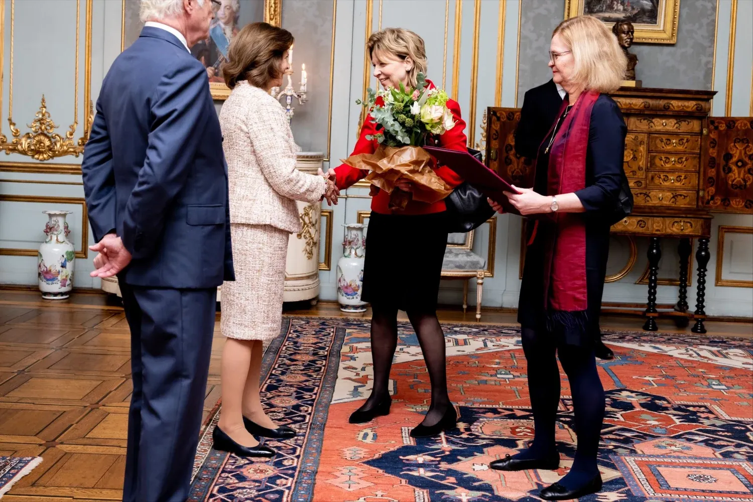 KI:s rektor överlämnar en gåva och blombukett till Drottningen. HMK står bredvid.