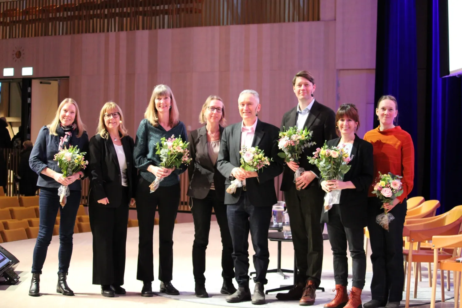 De medverkande har fått blommor som tack för dagens föreläsningar. Från vänster: Sara Hägg, Carin Lennartsson, Lena Dahlberg, Erika Jonsson Laukka, Jan C. Semenza, moderator Jens Berggren, Amaia Calderón-Larrañaga och Janne Agerholm som deltog i panelen.