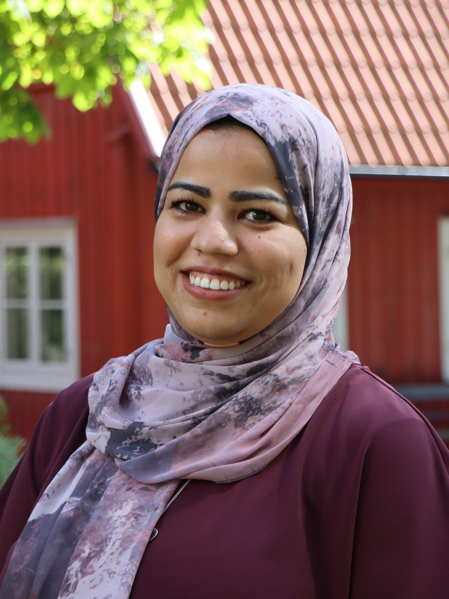 Porträtt av Heba Ali, doktorand vid avdelningen för neurogeriatrik, NVS, stående framför det röda gamla huset på KI Solnas Campus, mittemot Aula Medica.
