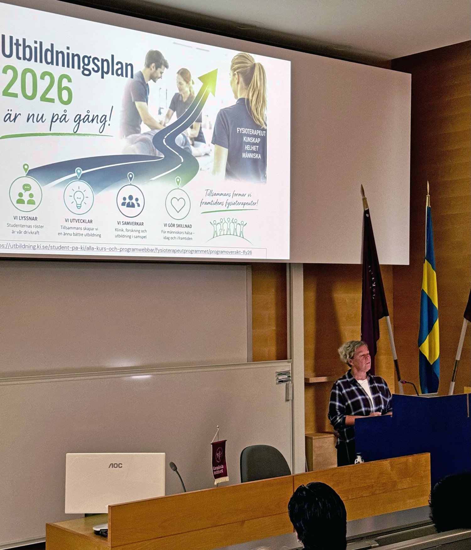 Marie Halvorsen står vid ett podie och pratar. På skärmen bakom henne syns en stor bild med utbildningsplan. Studenter i förgrunden.