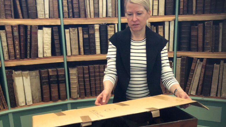 Ann Gustavsson står i ett bibliotek och öppnar en låda.