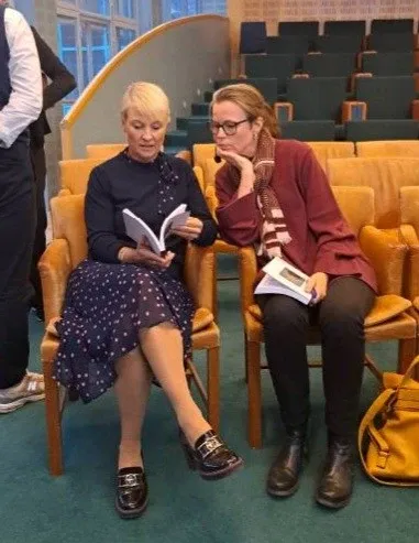 Isabelle von Saenger överlämnar sin doktorsavhandling till Anna Tenje. De båda sitter ner och Anna Tenje bläddrar i boken.