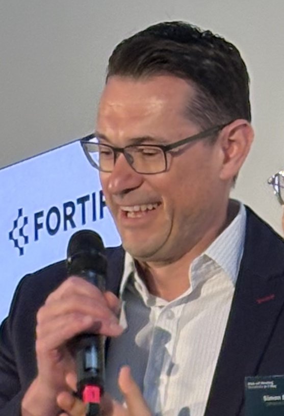 Två män står på ett podie under en konferens. De är glada.
