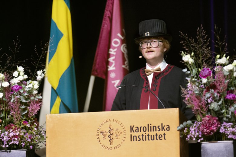 Brjánn Ljótsson står vid blomstersmyckat talarpodie och blickar ut mot publiken.