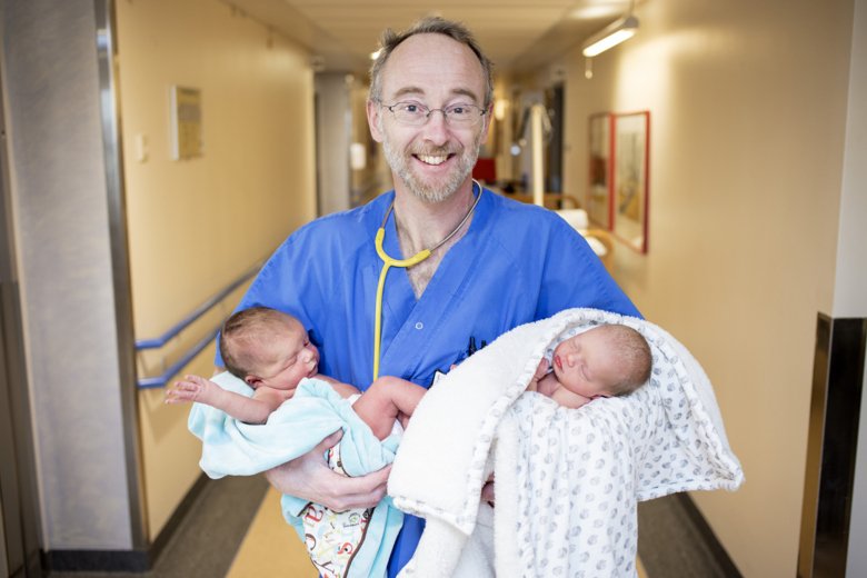 Porträtt av Jonas Ludvigsson klädd i sjukhuskläder med två bebisar i sin famn.