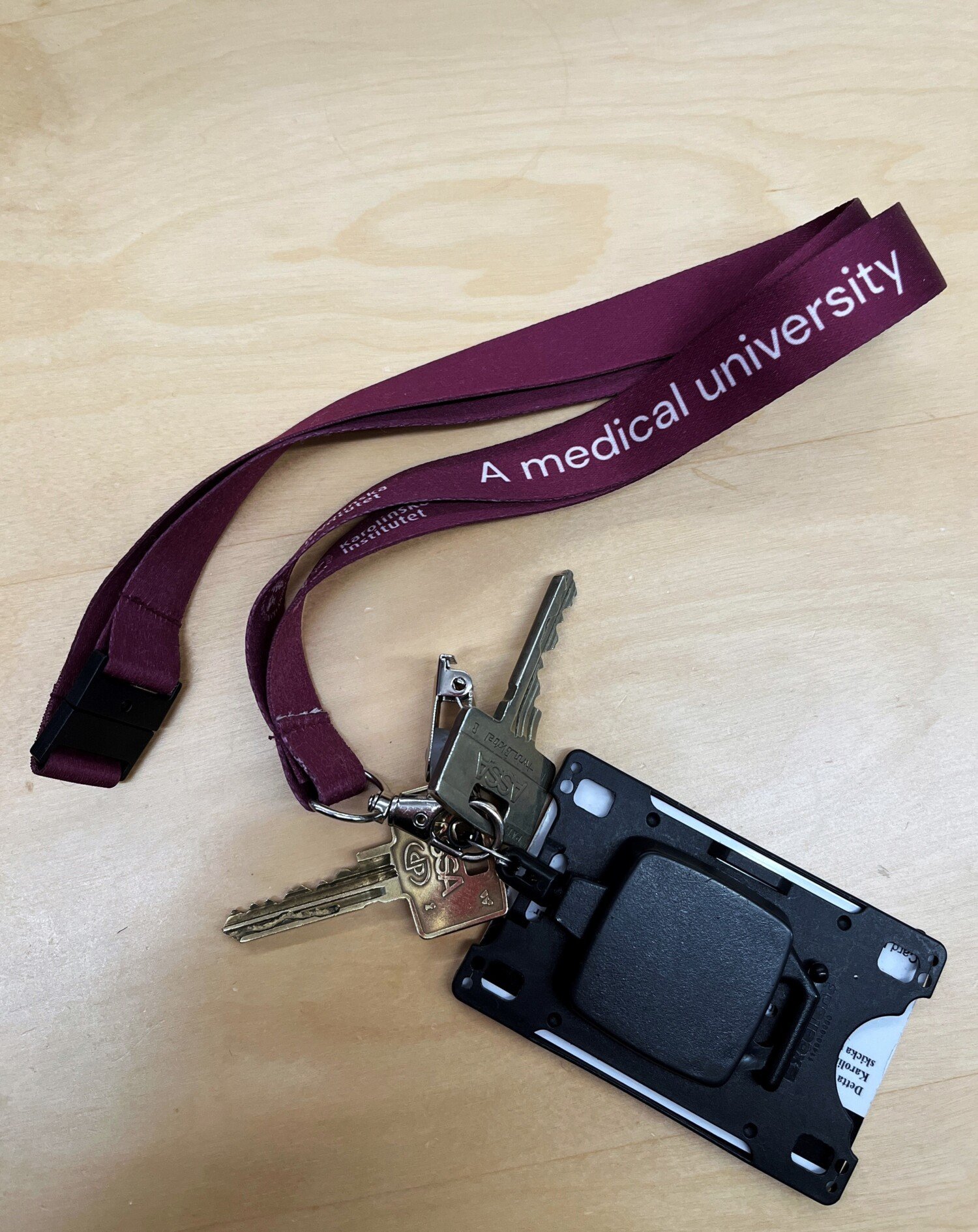 Två nycklar och ett passerkort i hållare, med nyckelband i KI:s plommonfärg.