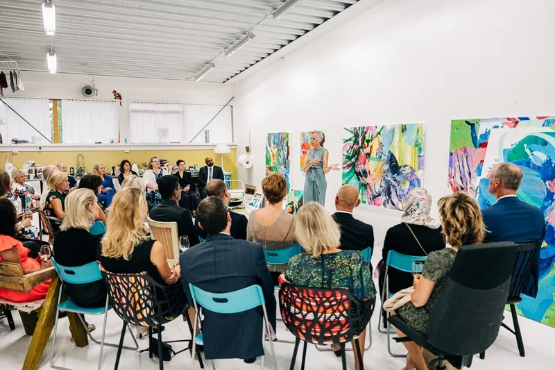 Bild på sittande människor som lyssnar på talande kvinna som står framför några tavlor.