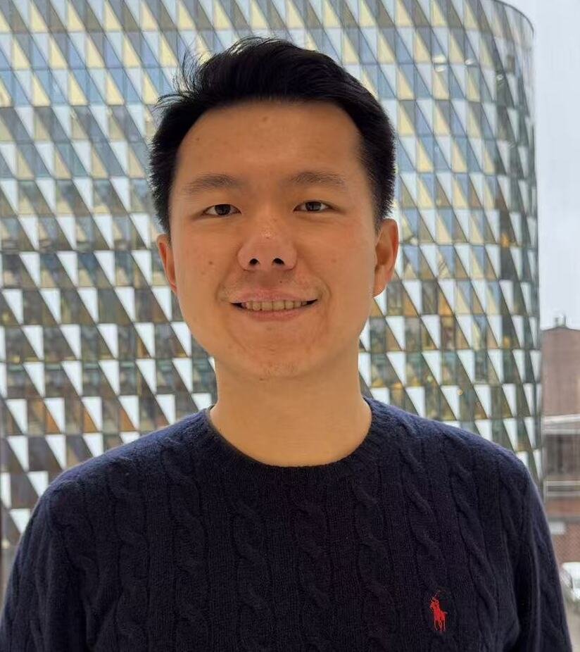 Mörkhårig man med blå tröja står med Aula Medica i bakgrunden.