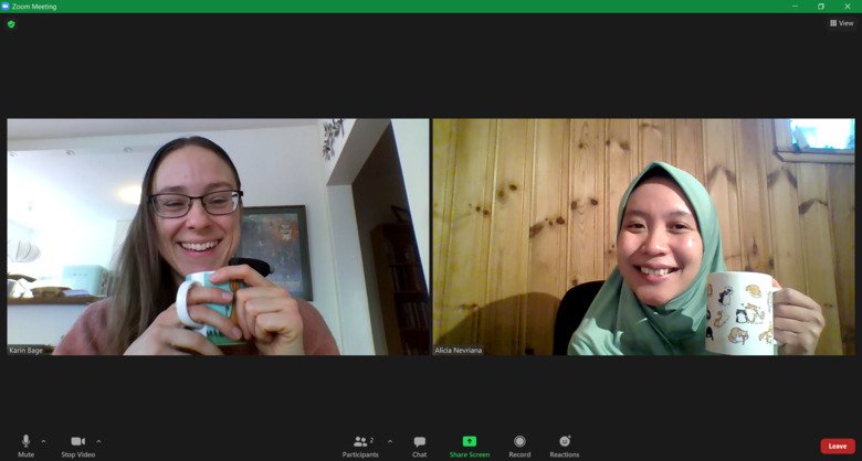 The PhD student representatives Alicia and Karin smiling to the camera with a coffee mug in hand, during an Zoom meeting.