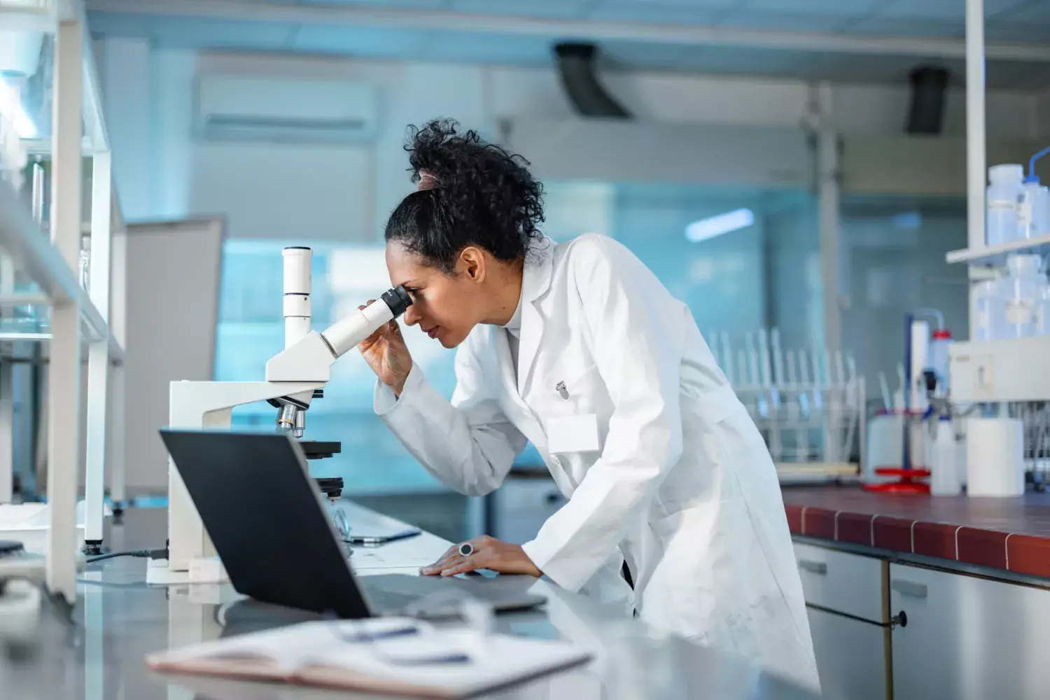 Kvinna på labb tittar i ett mikroskop.