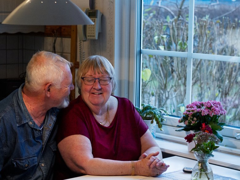 Äldre par sitter nära varandra vid bord intill fönster.