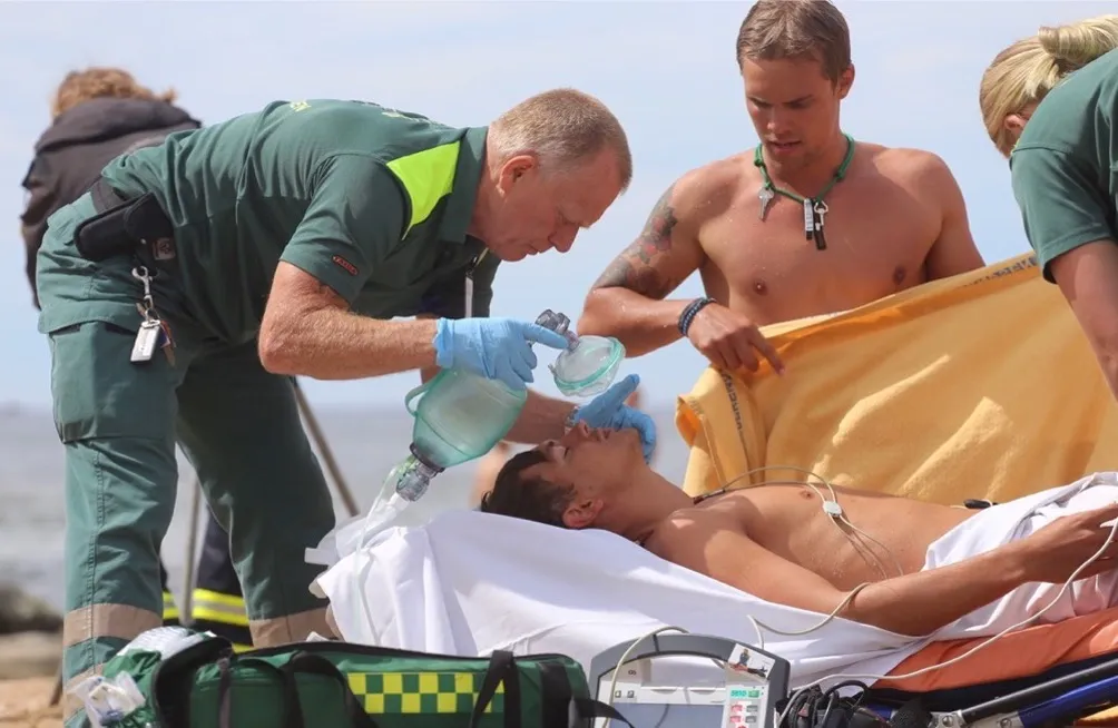 Ambulanspersonal och andra tar hand om en drunknad som ligger på en bår.