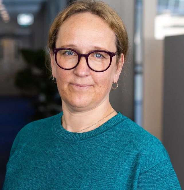 Porträtt av kvinna i blå tröja bredvid en växt.