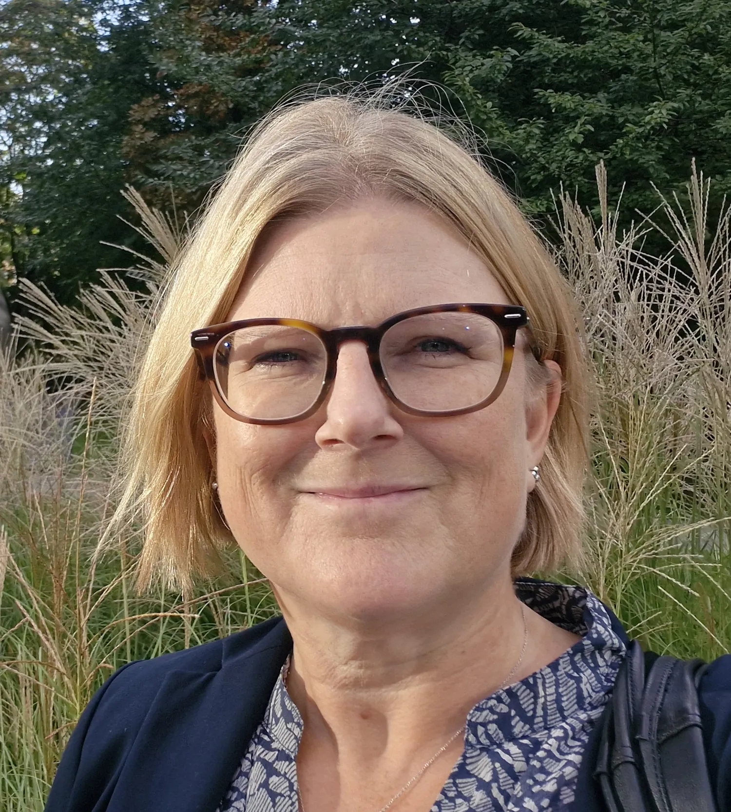 Porträtt på blond kvinna med glasögon, fotad utomhus.
