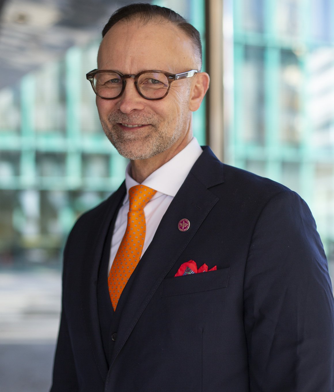 Porträtt av man i svart kavaj och orange slips.