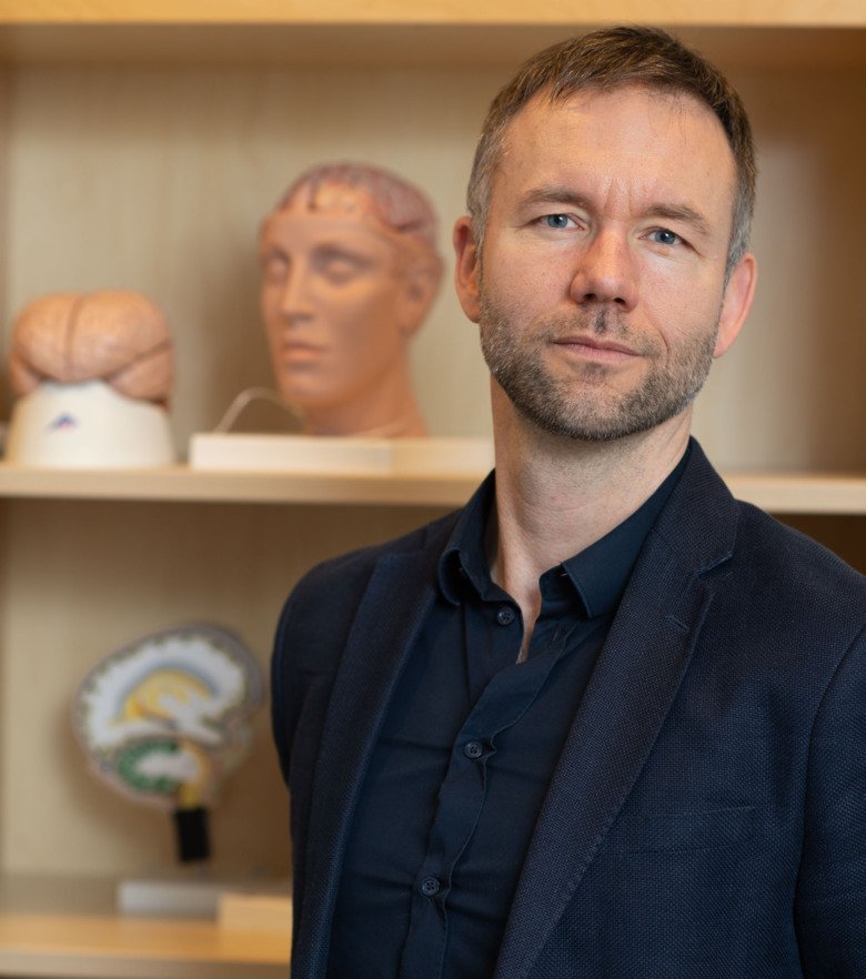 Porträtt av Andreas Olsson framför en hylla med modeller av huvuden, ansikten och hjärnor.