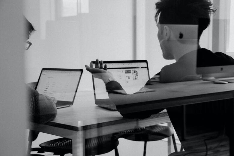 Två män sitter med varsin dator och diskuterar innehållet.