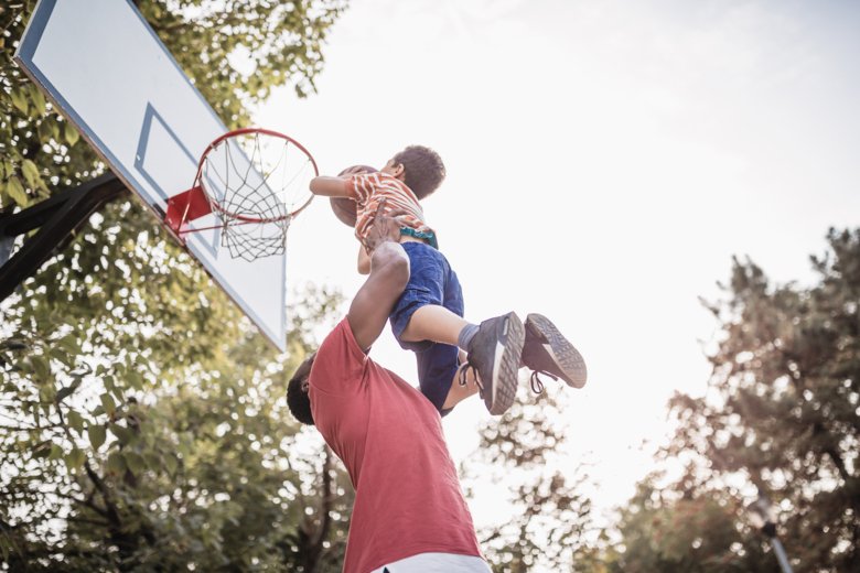 En pappa som lyfter sitt barn vid en basketkorg