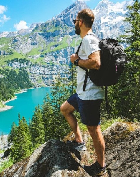 Student står med ryggen mot kameran och bär en svart ryggsäck. Han blickar ut över vacker natur med berg och vatten.