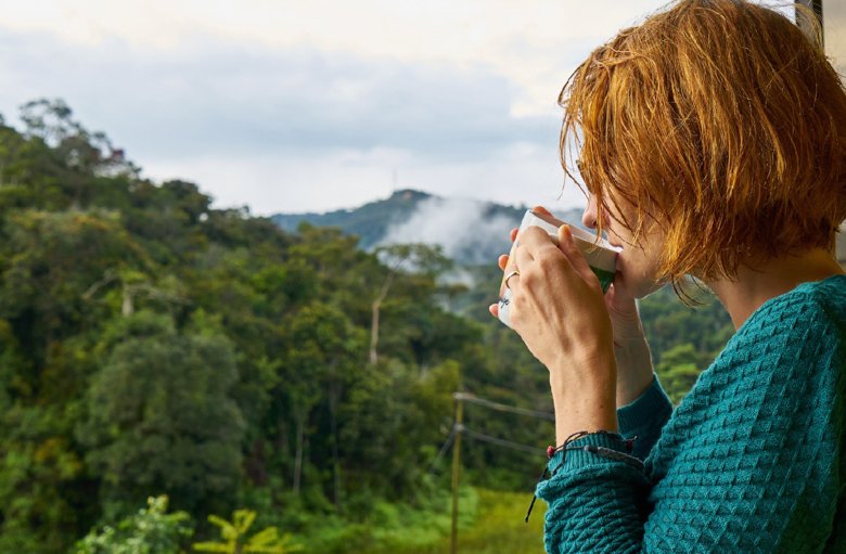 Kvinna som dricker kaffe och tittar ut över skogsområde